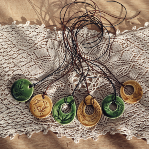 Ręcznie robiony ceramiczny wisiorek z odciśniętym roślinnym wzorem zawieszony na rzemieniu